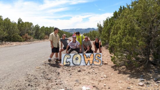 Students standing in front of a sign that says "Cows" in the desert