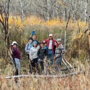 A group of Changemakers pose in fall colors while planting willows