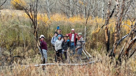 A group of Changemakers pose in fall colors while planting willows