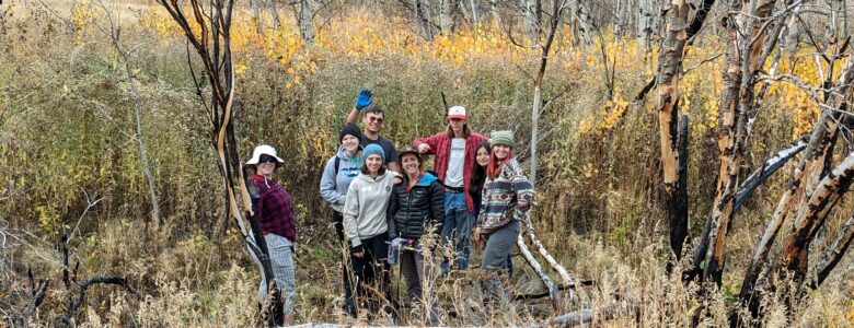 A group of Changemakers pose in fall colors while planting willows