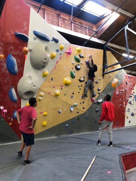 A Sims-Fayola participant works on a climbing project at The Spot while two others watch.