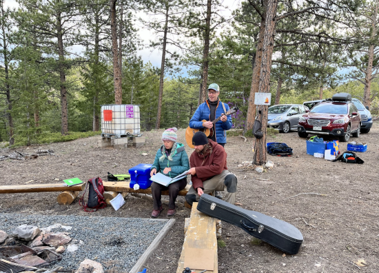 Three CI staff members at the campfire singing a song together. 