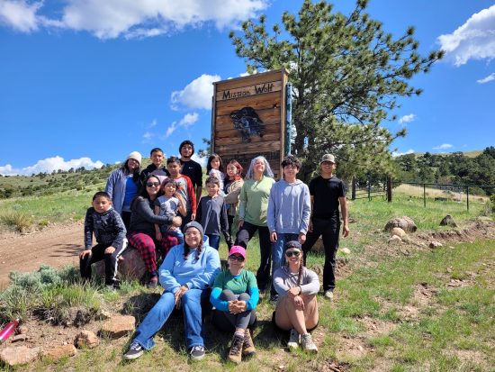 A group of Casa de la Esperanza students, parents, and instructors pose by the Mission: Wolf sign