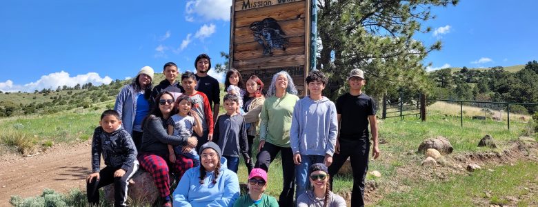 A group of Casa de la Esperanza students, parents, and instructors pose by the Mission: Wolf sign