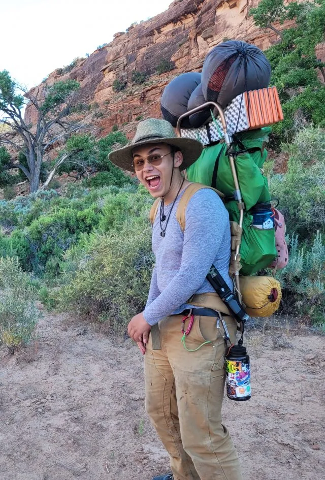 boy with rocks in the background smiling and carrying a big backpack