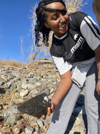 An AXL Academy 8th grade student picks up a rock while exploring Pelican Ponds Open Space