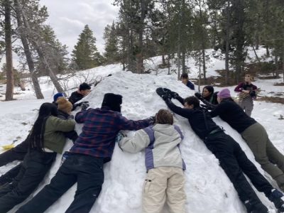 Students hug their snow shelter to solidifiy the walls before inserting sticks as width markers. They named the shelter “Juanito Pepito” Photo Courtesy of Ms. Llager, CLDE teacher.