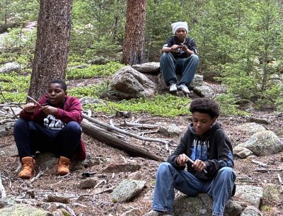 AXL 8th graders practice whittling sticks while waiting for their turn to climb vertical rock.
