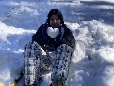 A Cottonwood Institute student displays a hear made from snow while sitting in the snow during a program.