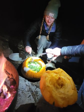 One Cottonwood alum stirs soup that is being cooked inside of a hallowed out pumpkin.