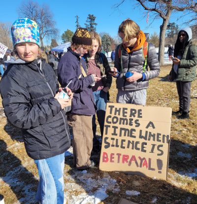 Cottonwood alumni gather in a small group near their handmade sign (focused on social justice) at the Denver MLK Day Marade.