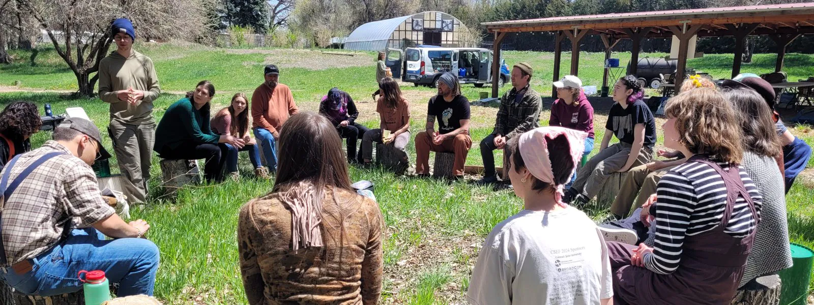 Attendees of the Ancestral Skills Gathering sit on stumps in a circle.