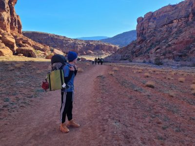 One member of the Big Blue Booty Bears enjoys a moment of backcountry magic as he looks at his backpacking companions and the red canyon walls in the distance.