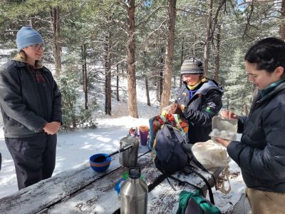 Changemakers Alumni get out stoves and food as they prepare to have brunch outdoors on a picnic table in the snow.