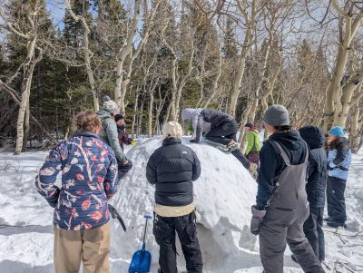 If you want to sleep in quinzees, you have to build them first! Students surround their snow shelter as one person climbs on top.