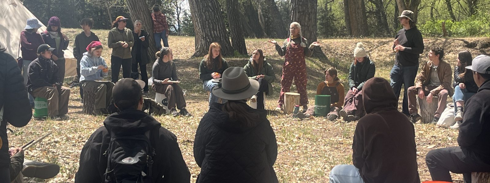 A Cottonwood Instructor speaks to the group of Ancestral Skills Gathering attendees, who are gathered in a circle.