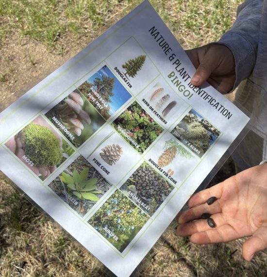 A student shows a nature identification bingo game board along with some items they found while camping.