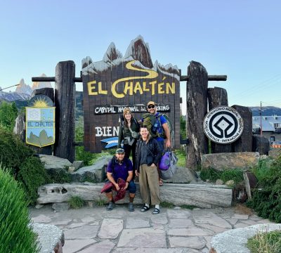 Cottonwood Board member, Alyssa, poses in front of an El Chaltén sign in Argentina with 3 other travelers.