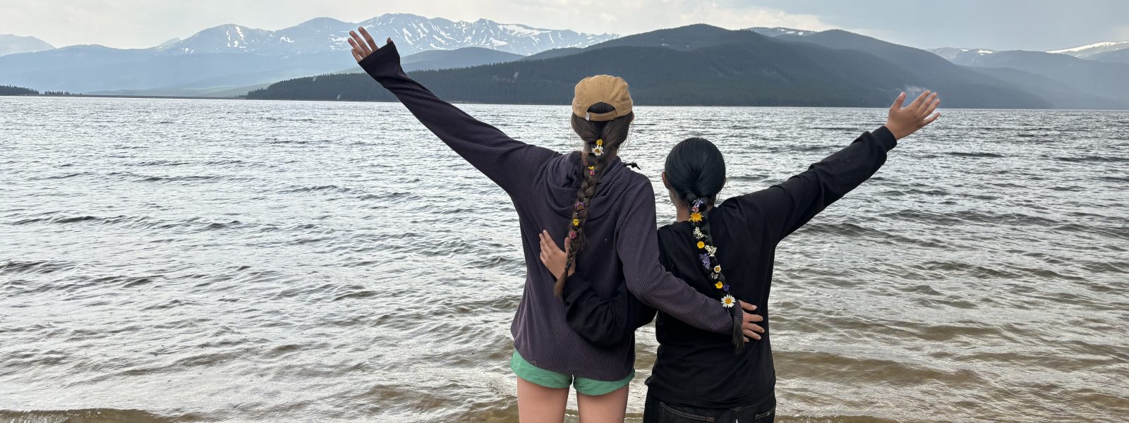 Two students stand in front of a large lake with their hands in the air during a Cottonwod Water Education program.