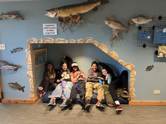Five AXL CAP students sit in a cozy spot surrounded by examples of local wildlife at Barr Lake Nature Center.