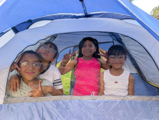 Four young children smile through the window in their camping tent.