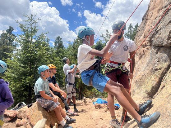 Students look on while one tests out the rope while rock climbing.