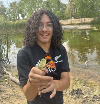 An AXL CAP alumni student holds a frog found during the alumni community fishing gathering.