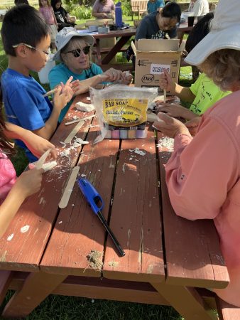 People sit at a picnic table while carving spoons at the ancestral skills workshop.