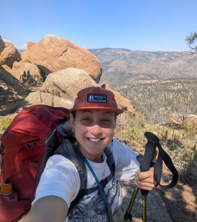 This Staff Spotlight focuses on Hannah, who poses while backpacking with a view of the mountains behind her.