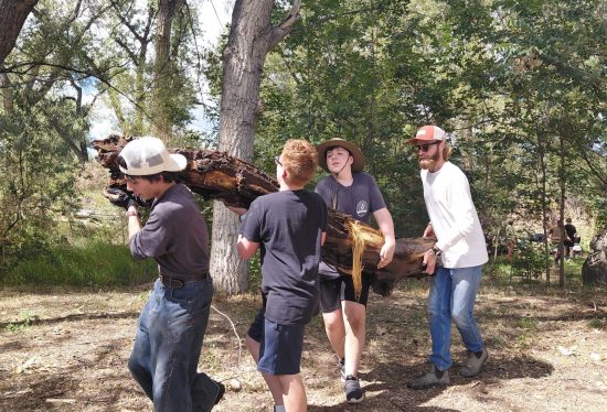 New Vista students and a teacher help haul a log during their regenerative farming focused field day trip.