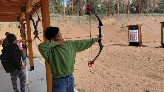 One AXL student aims a bow and arrow toward a target during their outdoor Wellness Day.