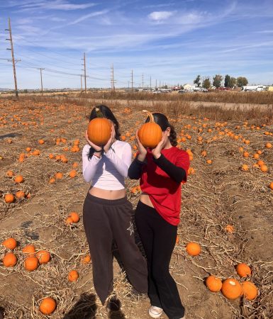 Two students pose with pumpkins in front of their faces during their farm-based learning day.