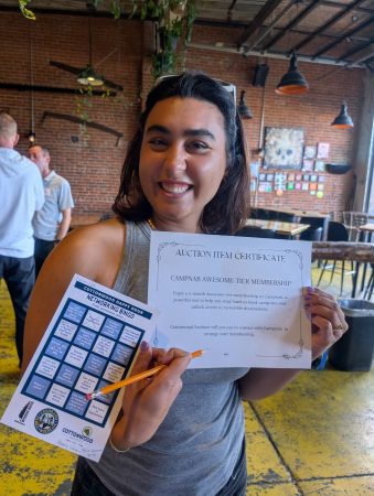 A community networking event attendee shows off a networking bingo card and a gift certificate she won at the event.